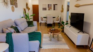 A living room with a sofa, coffee table, TV, and dining area with chairs and a table. - Apto a 280m da Praia do Itagu c Piscina e Garagem (Ubatuba)