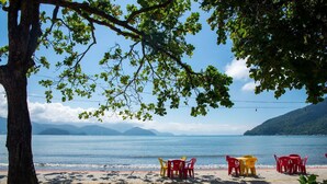 A beachside table and chairs with a view of the sea and mountains. - Apto a 280m da Praia do Itagu c Piscina e Garagem (Ubatuba)