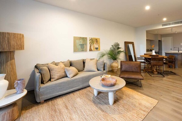 A modern living room with a sofa, coffee table, and a dining area with chairs and a table. - Byron Social on Jonson (Byron)