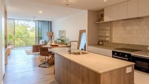 A modern kitchen with a central island, wooden flooring, and a view of the outdoors. - Byron Social on Jonson (Byron)