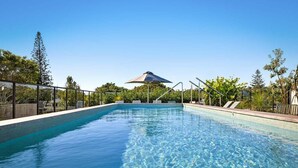 A clear blue pool with a metal railing, surrounded by trees and a clear sky. - Byron Social on Jonson (Byron)