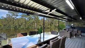 A covered outdoor dining area with a table and chairs, overlooking a body of water and forest.
