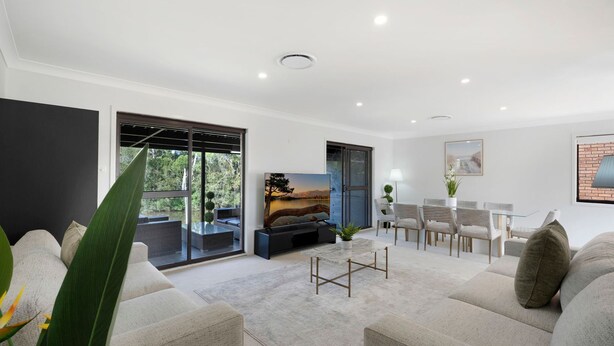 A modern living room with a large TV, comfortable seating, a dining area, and a view of the outdoors.