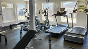 A gym with various exercise equipment, large windows, and a clock on the wall.