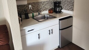 A compact kitchen with white cabinets, a microwave, a coffee maker, and a sink.