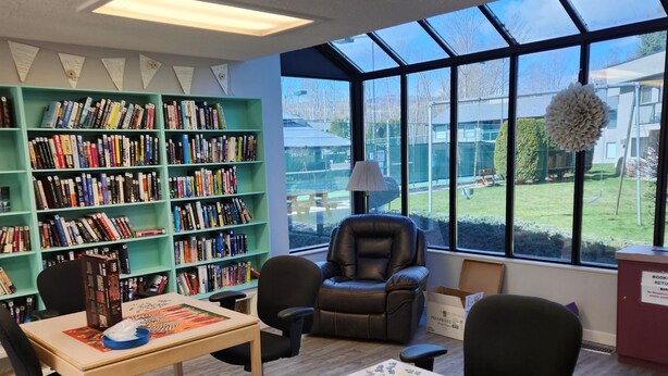 A library with bookshelves, a puzzle table, a leather chair, and large windows.