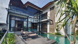 Ett modernt hus med en swimmingpool, ett trädäck och solstolar.