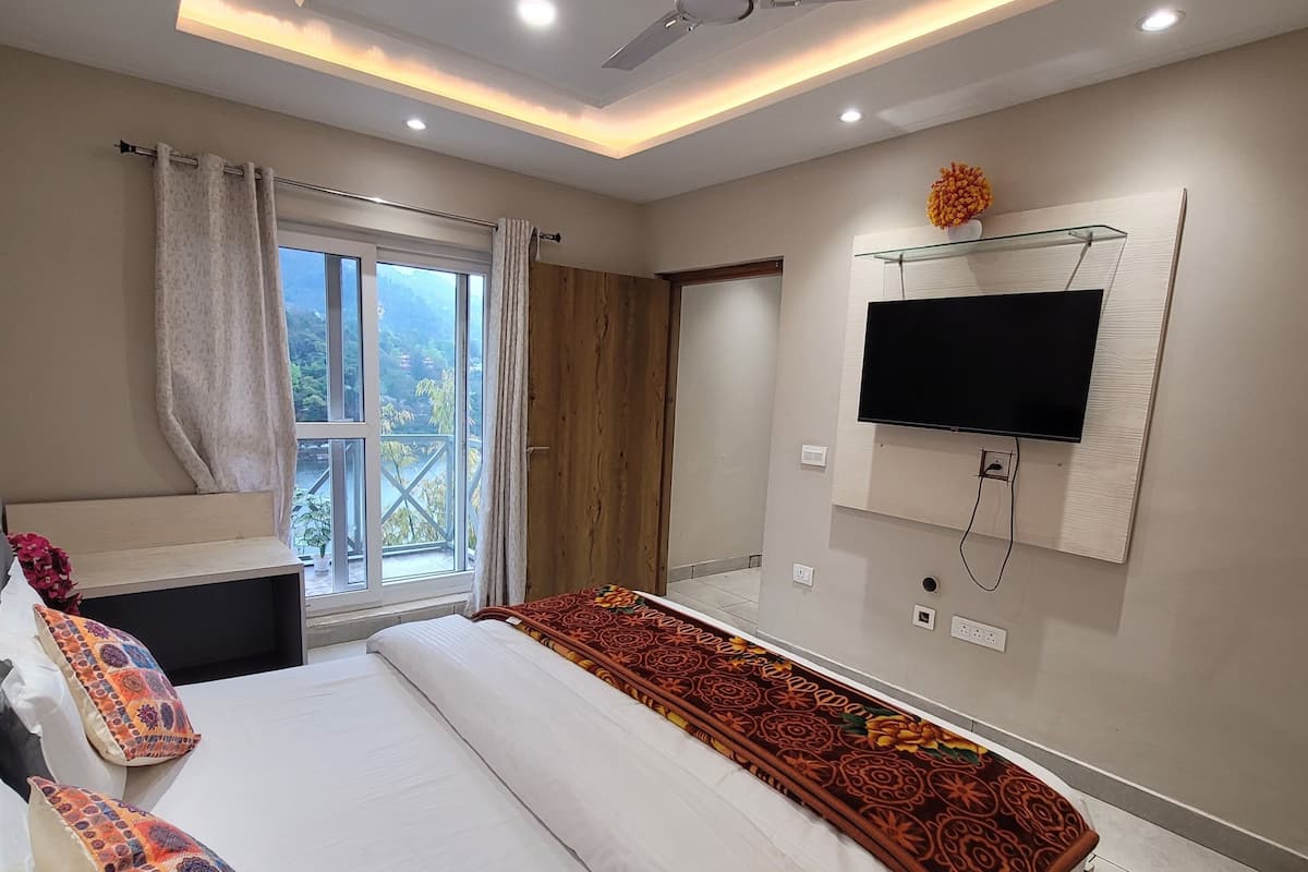 A modern bedroom with a large bed, a ceiling fan, a TV mounted on the wall, and a window with curtains.