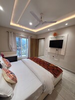 Un dormitorio moderno con una cama grande, ventilador de techo, televisor montado en la pared y una ventana con cortinas.