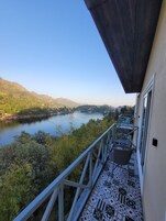 Un balcón con vistas a un lago y colinas, sillas de metal y baldosas de suelo estampadas.