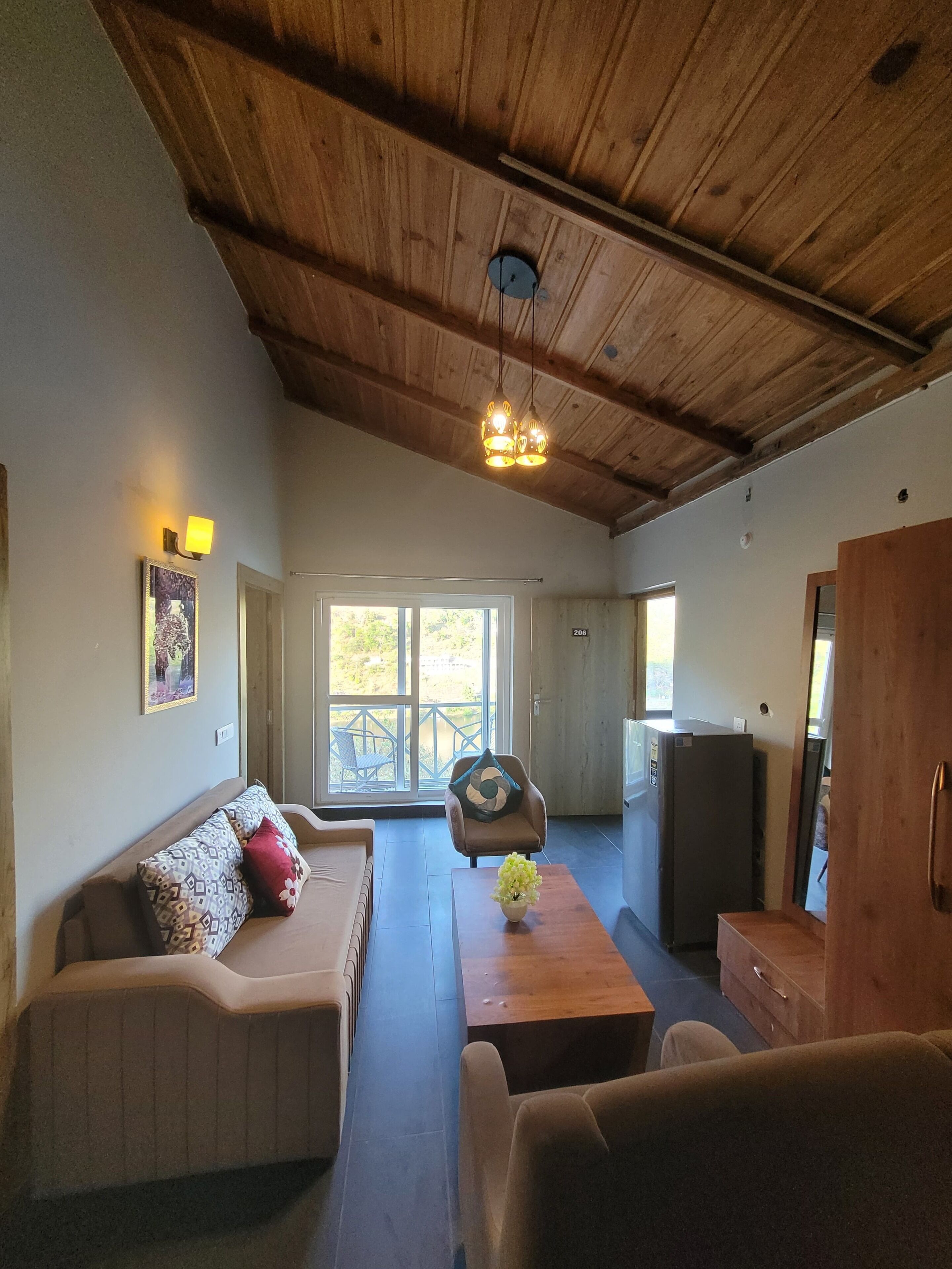 Un salon chaleureux avec un plafond en bois, un canapé, une table ornée d’un vase et une vue à travers une porte vitrée.