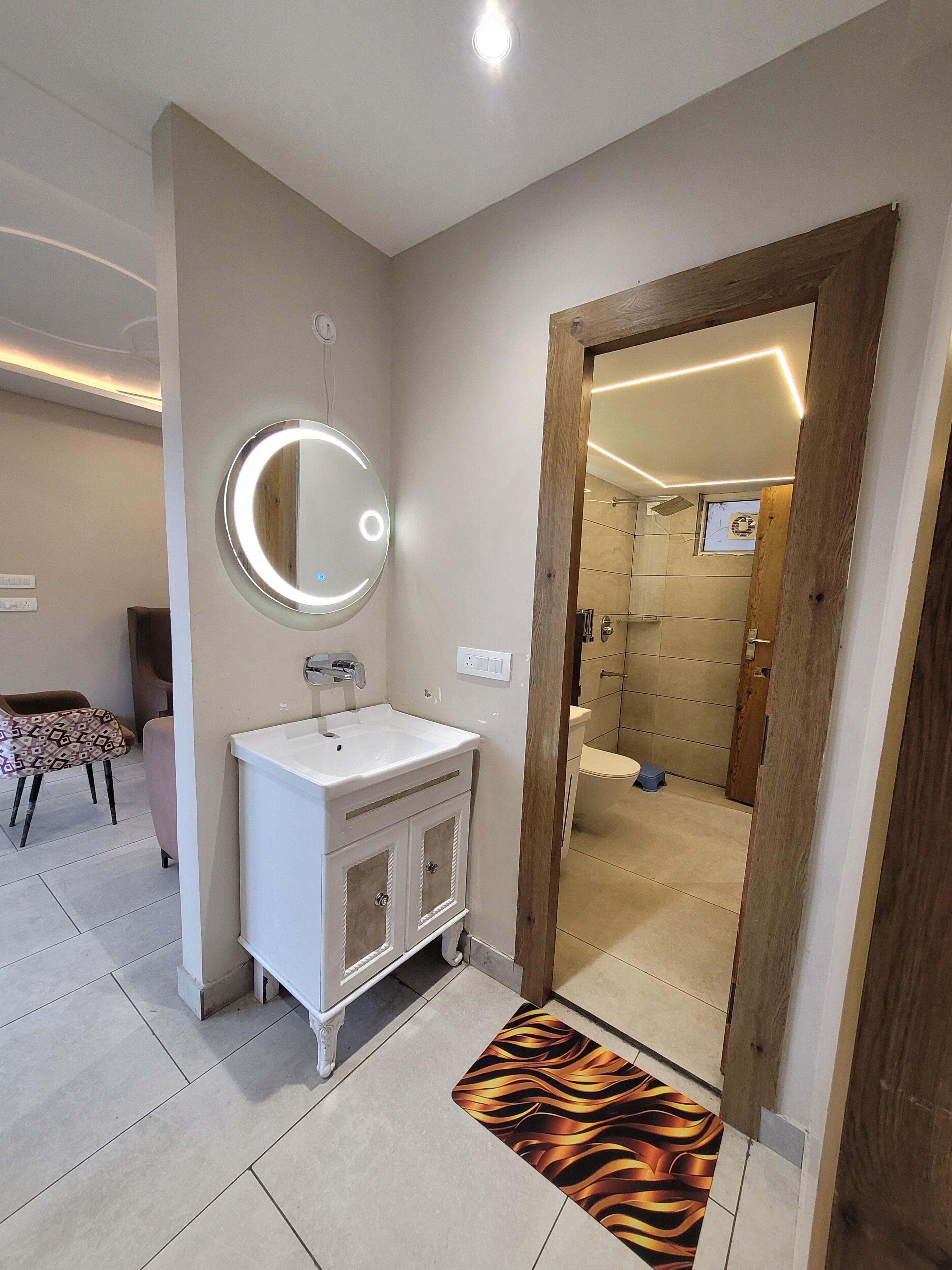 Een badkamer met een witte wastafel, spiegel en een houten deur naar een douchecel.
