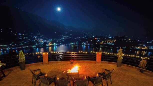 Una terraza con una chimenea, sillas y vistas a un paisaje urbano nocturno.