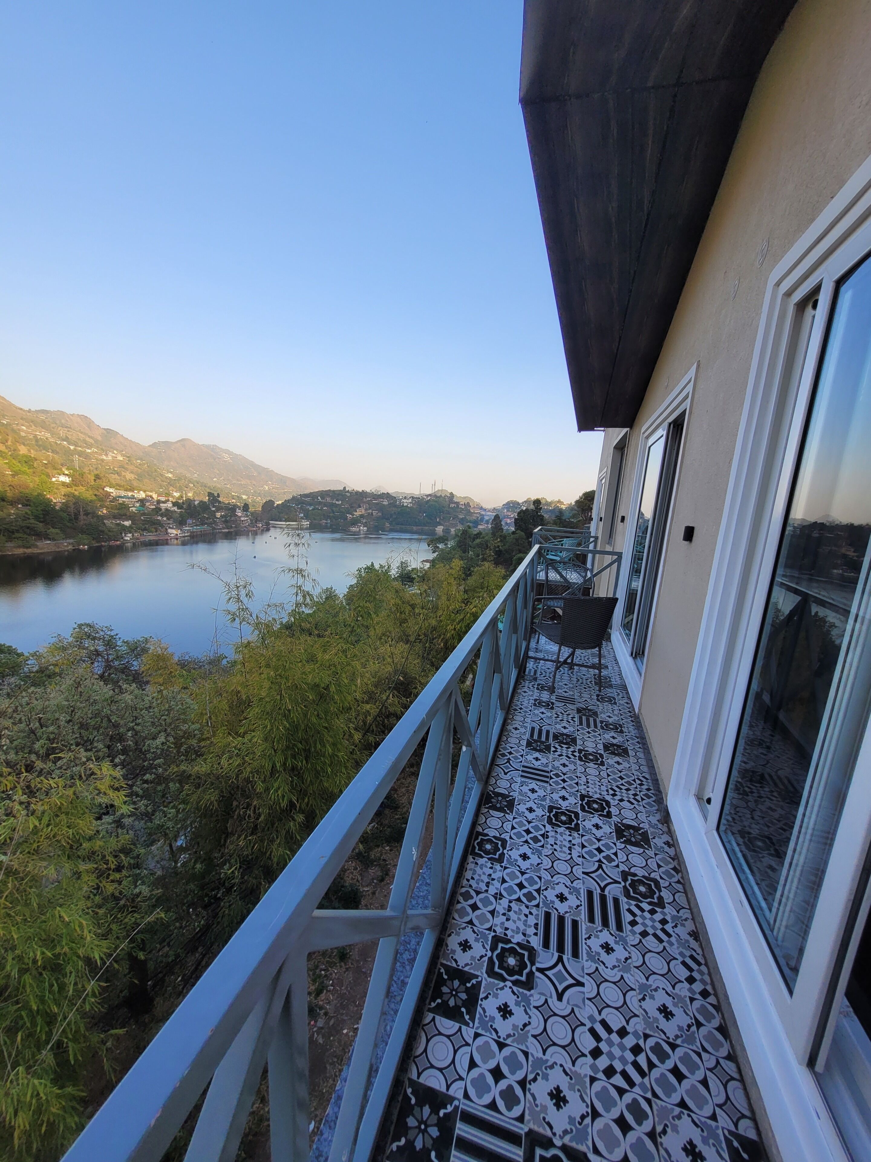 Ein Balkon mit gemustertem Boden, einem Geländer und Blick auf einen See und Hügel.