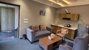 Una sala de estar moderna con sofá, sillón, mesa de centro y una zona de cocina con refrigerador y lavamanos.