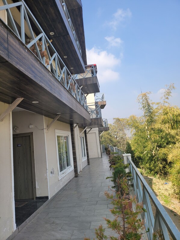 A multi-story building with a balcony, a door marked '102', and a pathway leading to a gate. - RnR Premium Stay (Bhimtal)