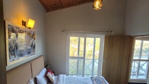 Un dormitorio con una cama grande, techo de madera, una ventana y una lámpara fijada a la pared.