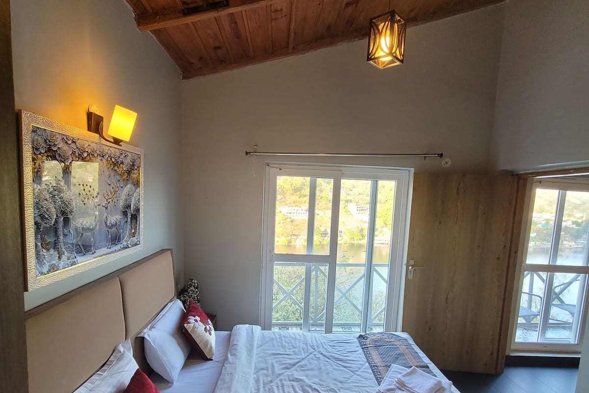 A bedroom with a large bed, a wooden ceiling, a window, and a wall-mounted lamp.