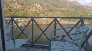Un balcón con sillas de mimbre que da a un lago, rodeado de colinas y edificios.