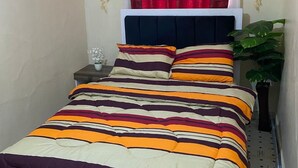 Une petite chambre à coucher, bien rangée, avec un lit, une table de chevet, une fenêtre ornée de rideaux rouges et une plante en pot.