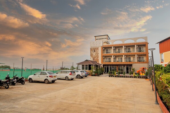 A hotel with a multi-story structure, a parking area with several cars, and a well-maintained garden.