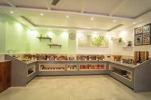 A modern, well-lit café with a green wall, shelves with food items, a clock, and framed pictures. - Ritz Valley Resort (Mahabaleshwar)