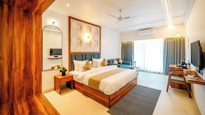 A modern hotel room with a large bed, a desk, a chair, a TV, and a ceiling fan. - Ritz Valley Resort (Mahabaleshwar)