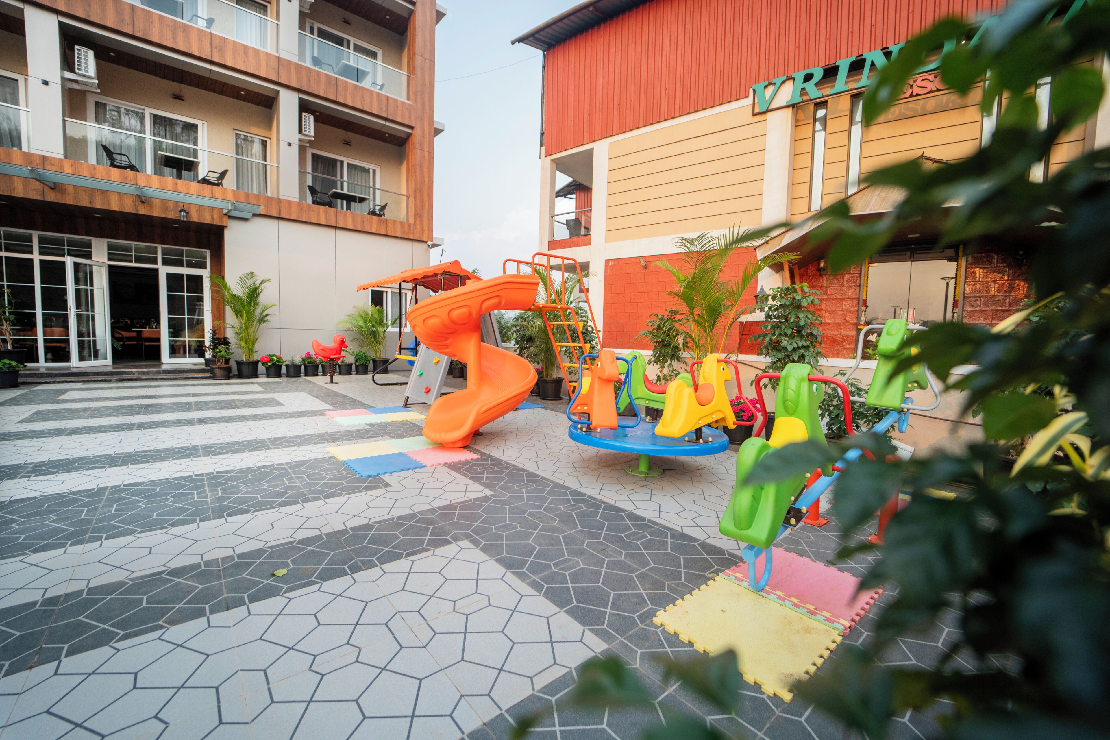 Un parque infantil con diversos juegos, un edificio con varios balcones y un suelo de baldosas.