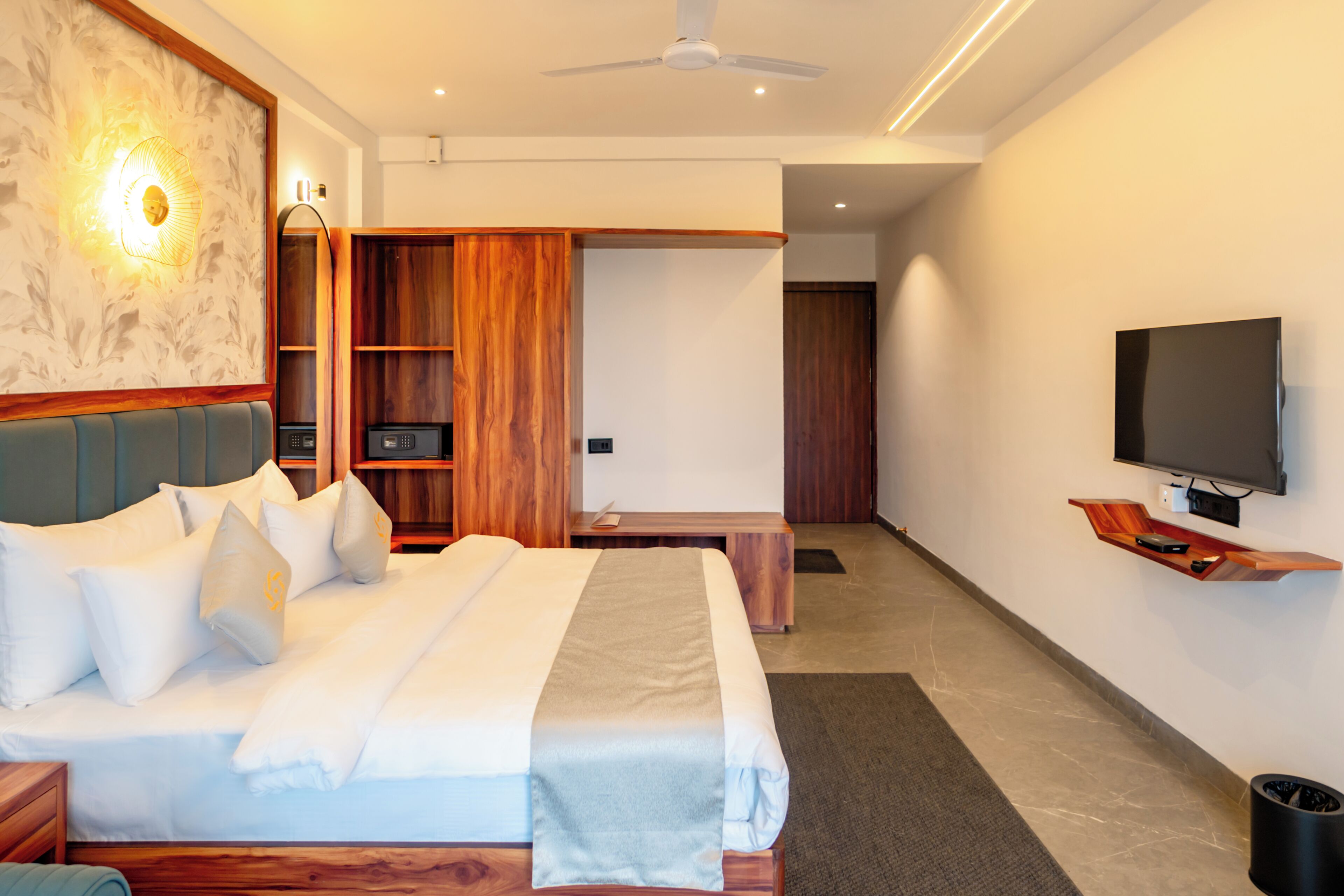 Una habitación de hotel moderna con una cama grande, televisión, armario de madera y ventilador de techo.
