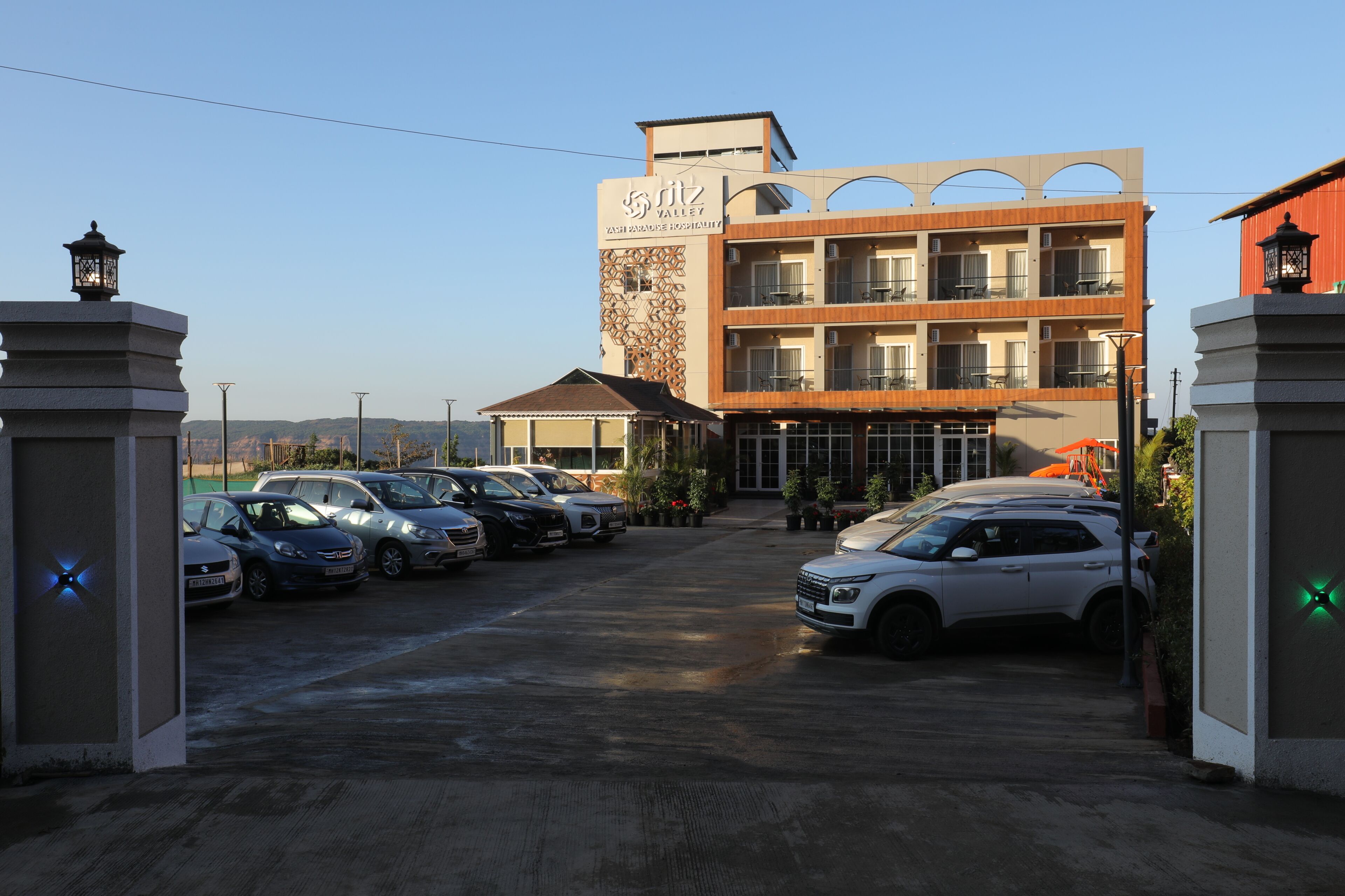 A hotel with a modern design, a parking lot with several cars, and a clear sky.