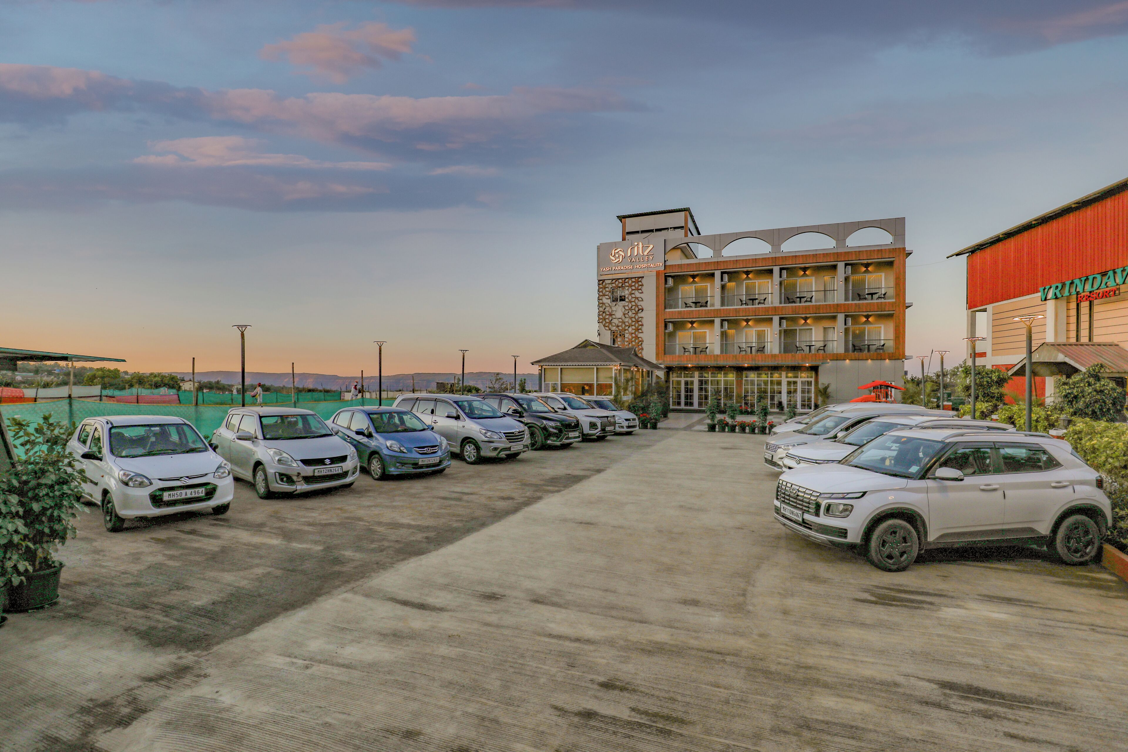 Un hôtel à plusieurs étages, un parking avec plusieurs voitures et un ciel dégagé.