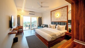A modern hotel room with a large bed, a desk, a television, and a balcony with a view. - Ritz Valley Resort (Mahabaleshwar)