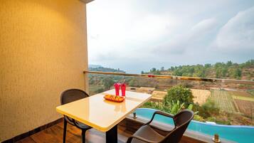 A balcony with a table and chairs, a view of a swimming pool, and a distant landscape.