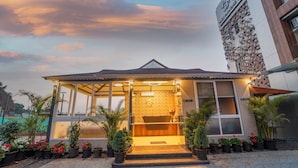 A hotel entrance with a covered porch, potted plants, and a modern building in the background. - Ritz Valley Resort (Mahabaleshwar)