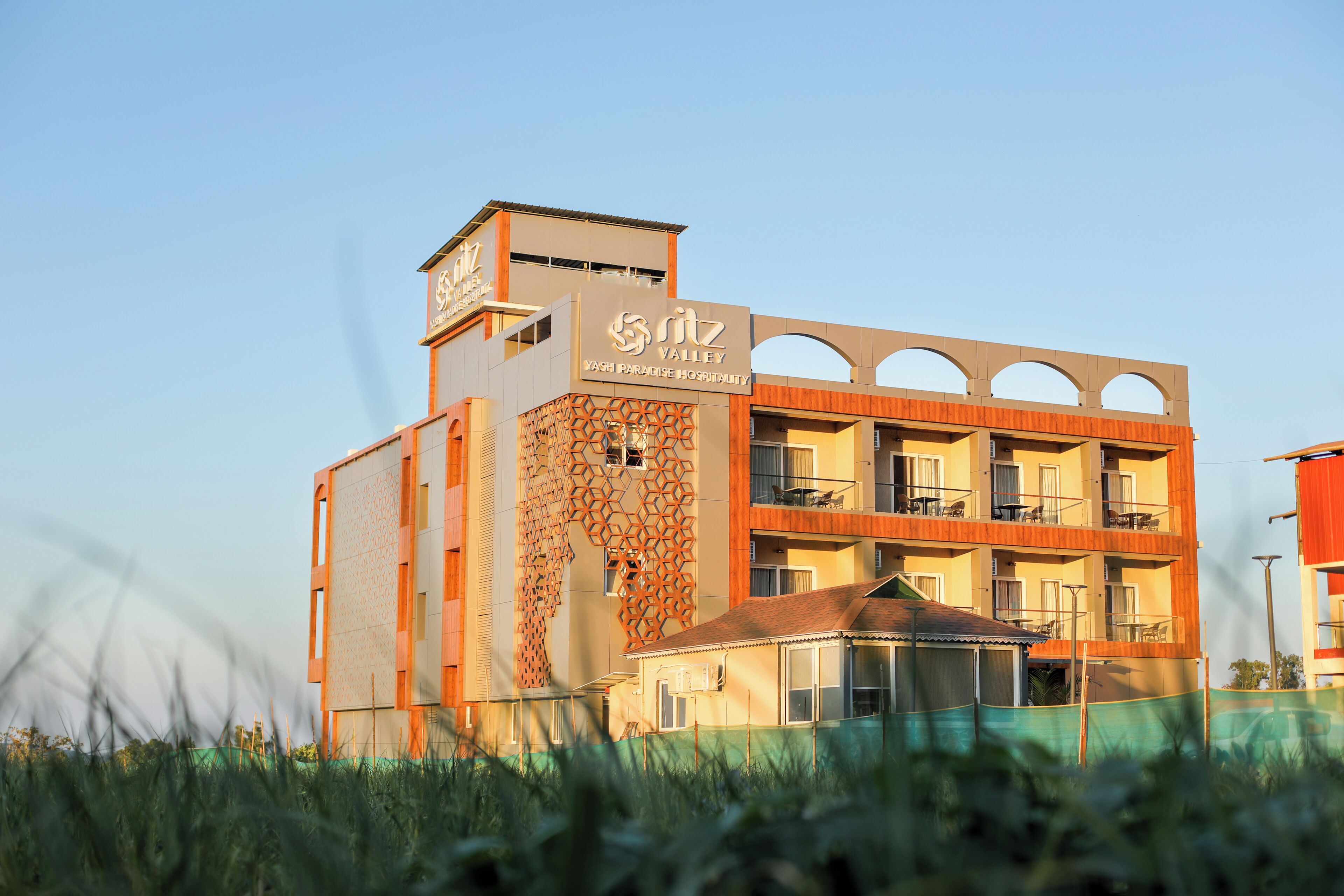 A multi-story hotel with a distinctive geometric facade, balconies, and a sign indicating it is a 'Yash Paradise Hospitality' establishment.