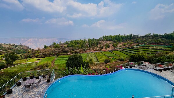 A pool with a view of terraced fields and a distant mountain range. - Ritz Valley Resort (Mahabaleshwar)
