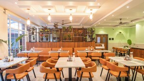 A restaurant interior with booths, tables, orange chairs, potted plants, and ceiling lights. - Ritz Valley Resort (Mahabaleshwar)