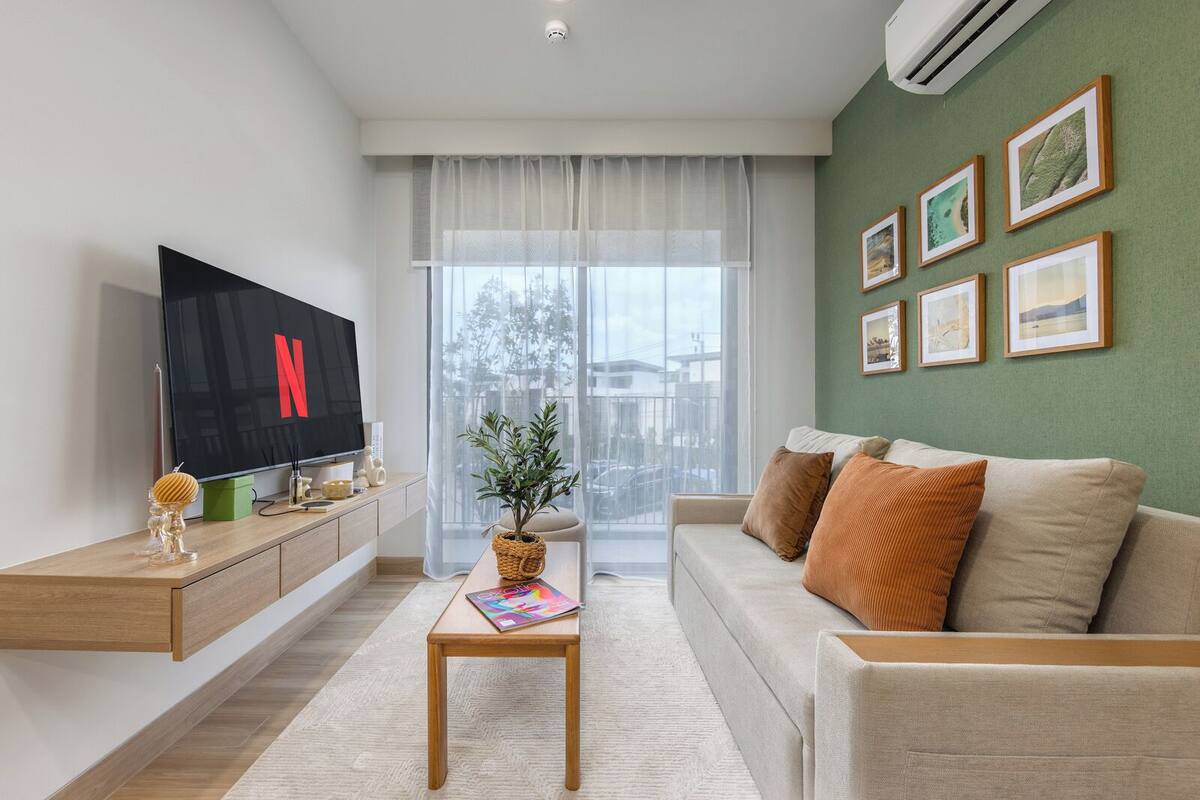 Una sala de estar moderna con un televisor de pantalla plana, un sofá, una mesa de centro y una pared verde decorada con cuadros.