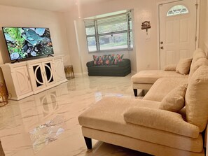 A living room with a TV, a sofa, a cabinet, and a window with blinds. - Casa las Brisas, with an outdoor hot tub and a lovely place to relax  (Lehigh Acres)