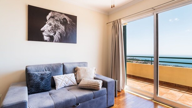 Una habitación con un sofá gris, un ventanal con vistas al mar y un ventilador de techo.