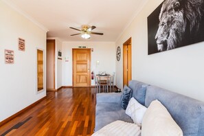 Ein Flur mit Deckenventilator, Holzboden, einem grauen Sofa mit Kissen und einem gerahmten Bild an der Wand.