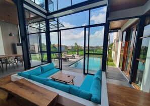 A modern interior with a large glass wall, a pool, and a seating area. - Casa Esquina - East Wing (Canggu)