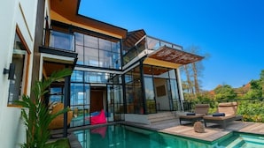 Ein modernes Haus mit Glasfassade, Swimmingpool und Sitzgelegenheit im Freien.