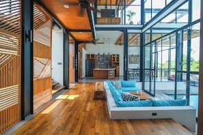 A modern interior with a wooden floor, a white sofa, and a glass wall overlooking a pool. - Casa Esquina - East Wing (Canggu)
