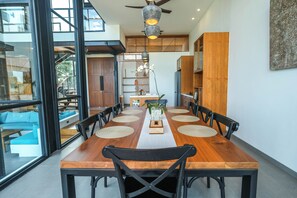 A dining area with a wooden table, black chairs, and a view through large windows. - Casa Esquina - East Wing (Canggu)