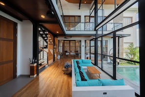 A modern interior with a wooden floor, a large window, and a pool visible outside. - Casa Esquina - East Wing (Canggu)