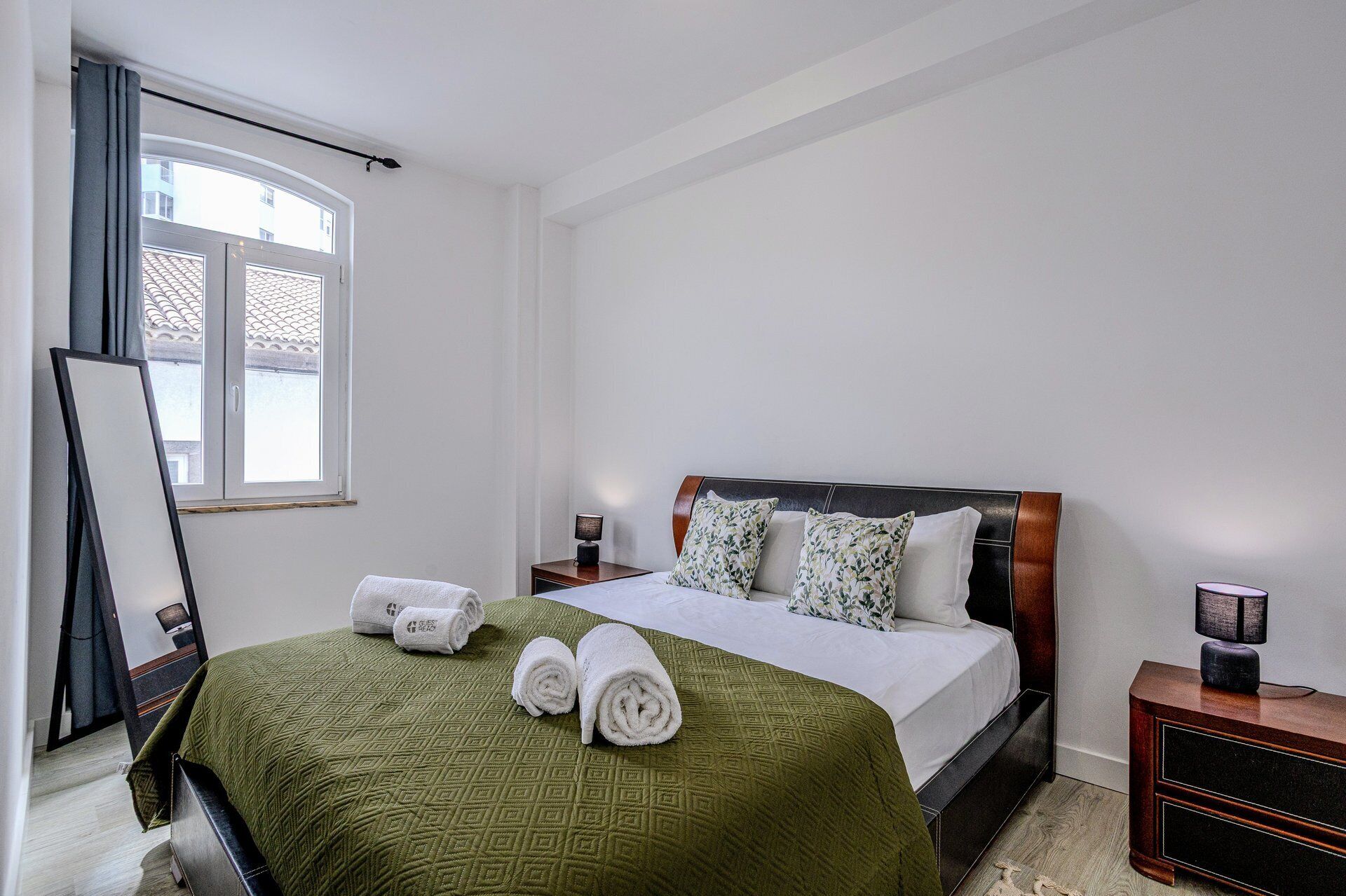 Una cama bien hecha con una colcha verde, dos almohadas y toallas enrolladas.