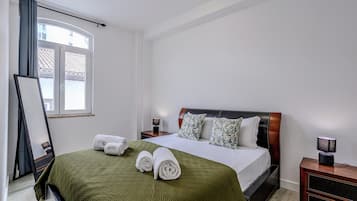 Una cama bien hecha con una colcha verde, dos almohadas y toallas enrolladas.