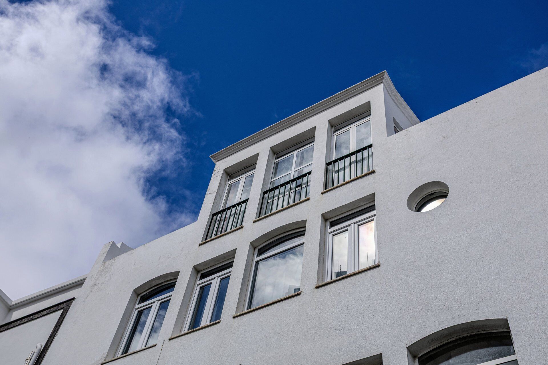 Un edificio de varios pisos con fachada blanca, numerosas ventanas y balcones.