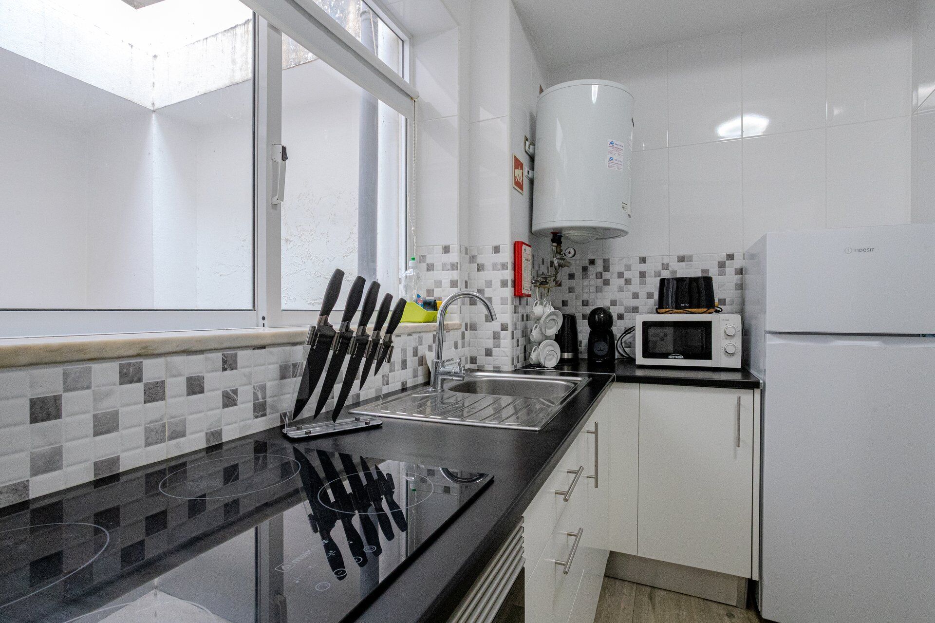 Una cocina moderna con encimera negra, pileta de acero inoxidable y muebles de cocina blancos.